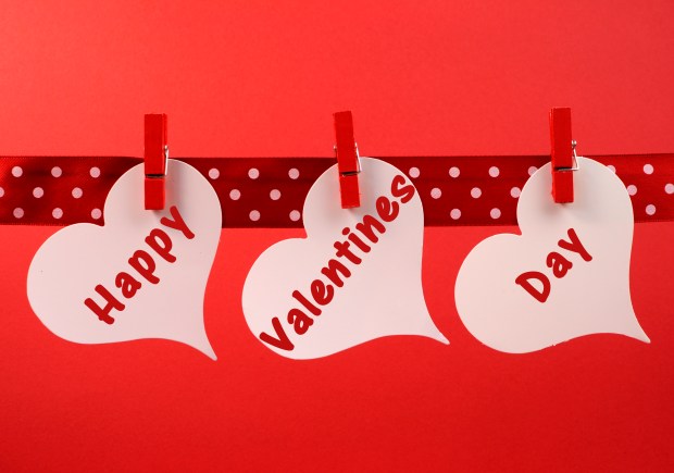 Happy Valentines Day message greeting written across white heart tags hanging from red pegs on a line for Valentines Day, February 14.